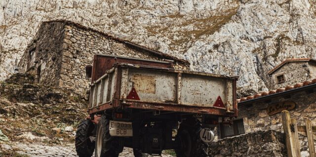 Old tractor parked near stone buildings in mountains