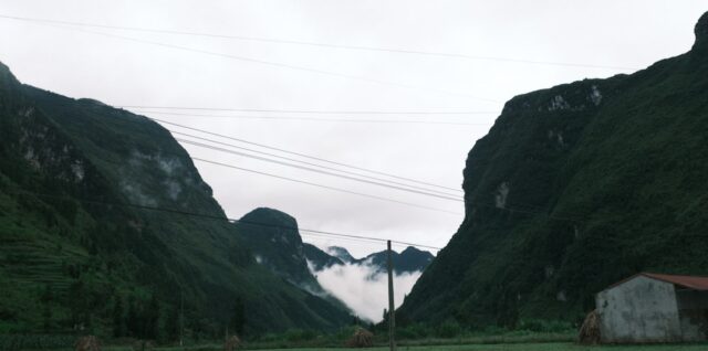a field with a house and mountains in the background
